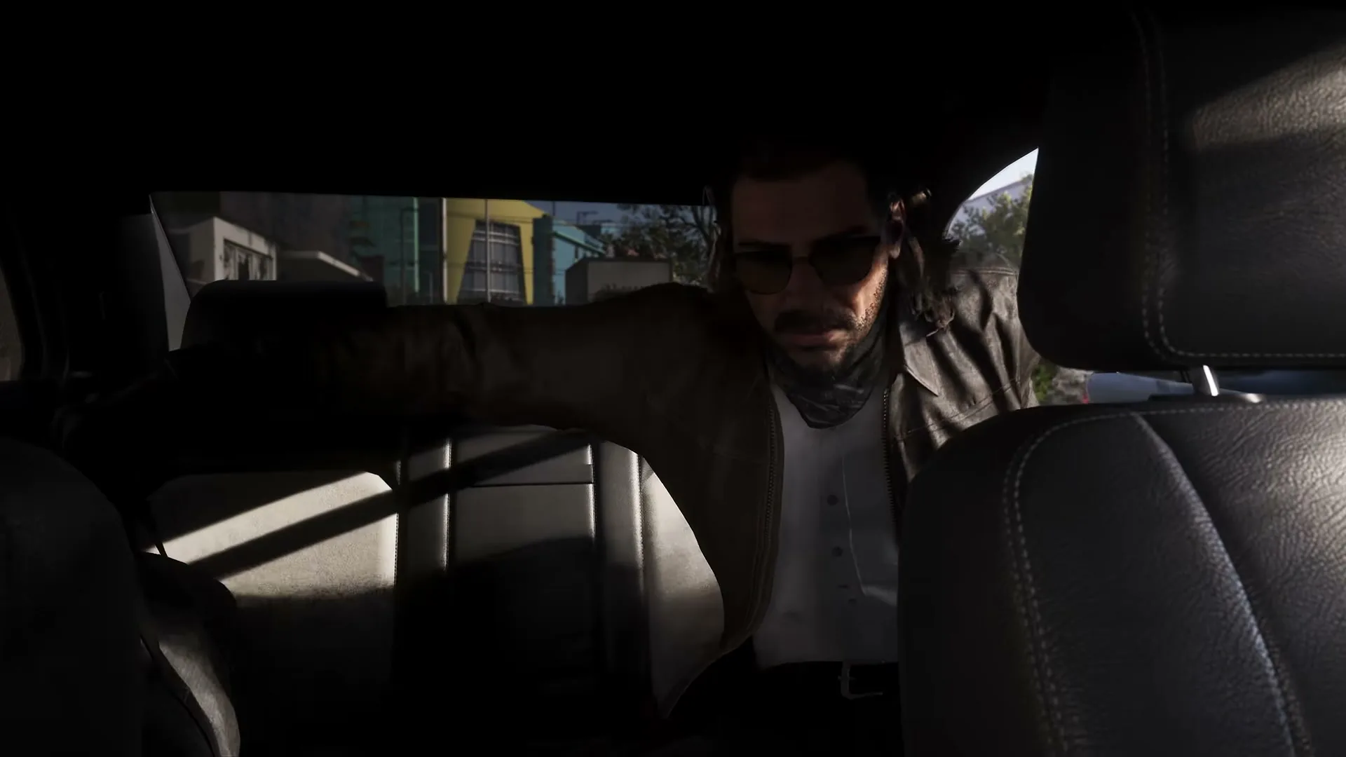 Raul Bautista leaning forward from the back seat of a getaway car, sunglasses on.
