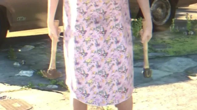 Person in a floral dress holding a hammer in each hand on a driveway, from the first official GTA 6 trailer