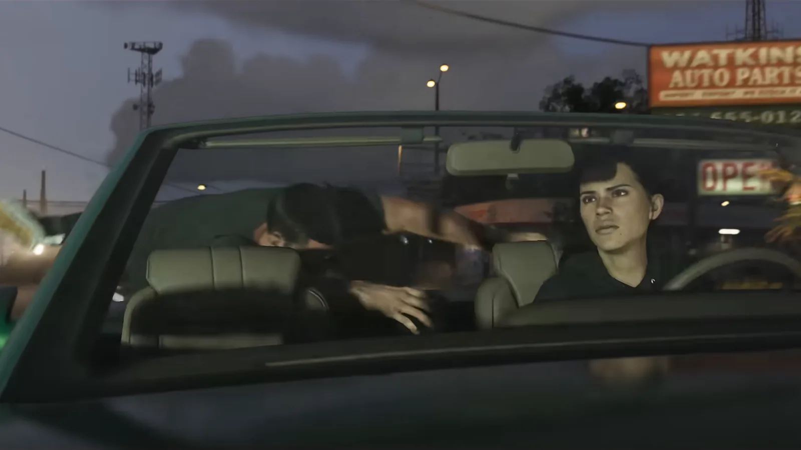Jason and Lucia ducking low in a convertible at dusk, from Trailer 2.